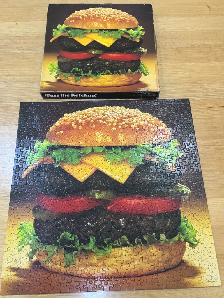 A double-decker cheeseburger with lettuce, tomato, and pickles centered against a dark, moody background.