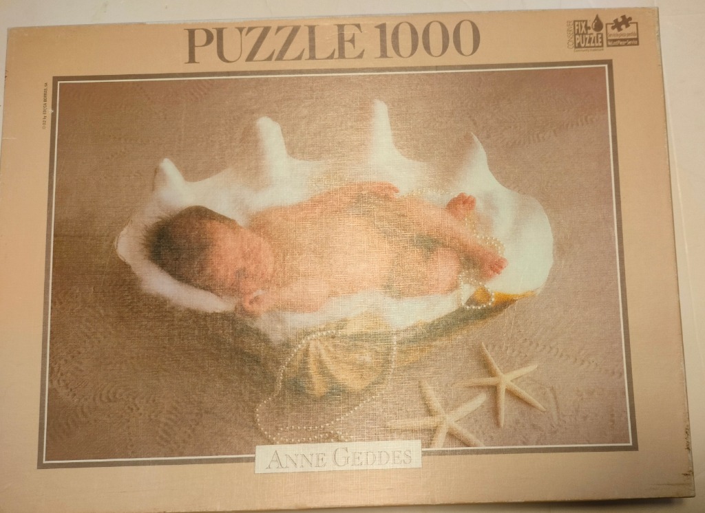 A newborn baby sleeping inside a large white seashell on a sandy surface with starfish and pearls.