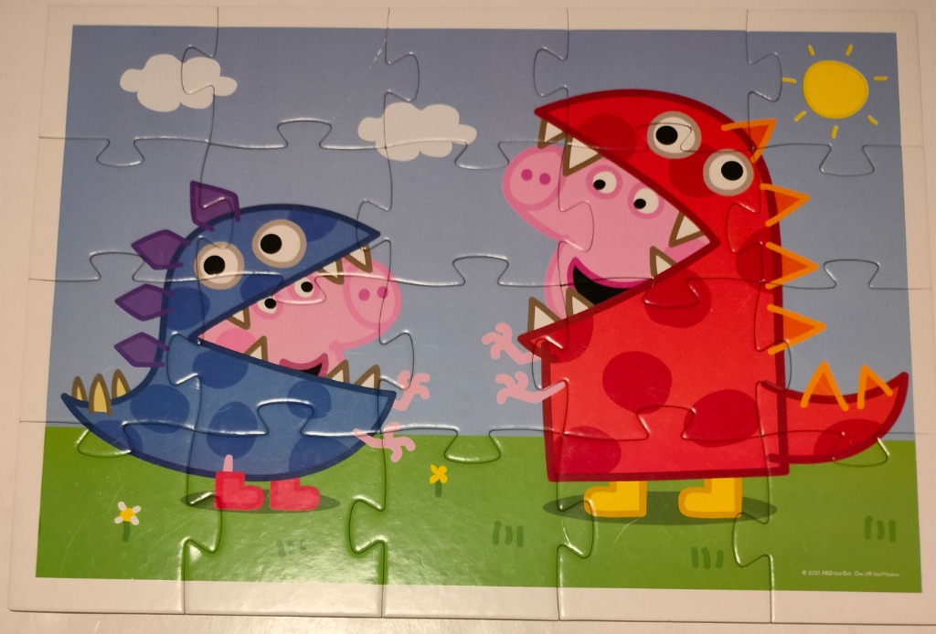 Peppa Pig and George Pig dressed in colorful dinosaur costumes in a green meadow under a blue sky.