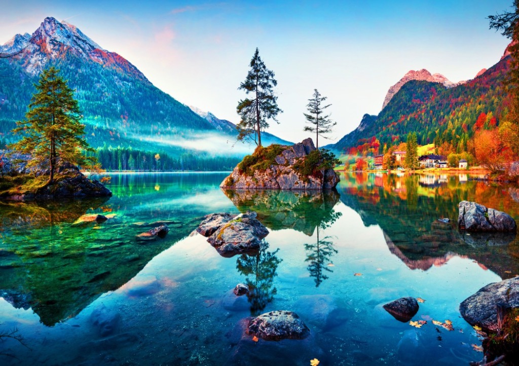A serene alpine lake featuring a rocky island with two trees, reflecting mountains and colorful autumn foliage.