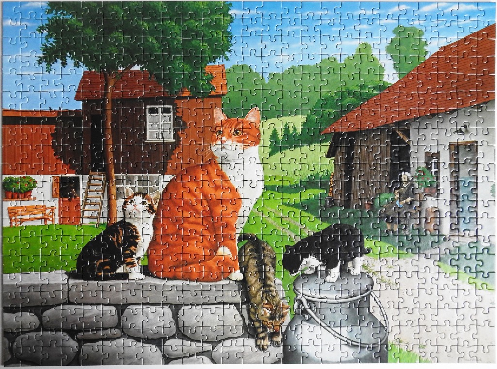 Four cats on a stone wall in a farmyard setting.