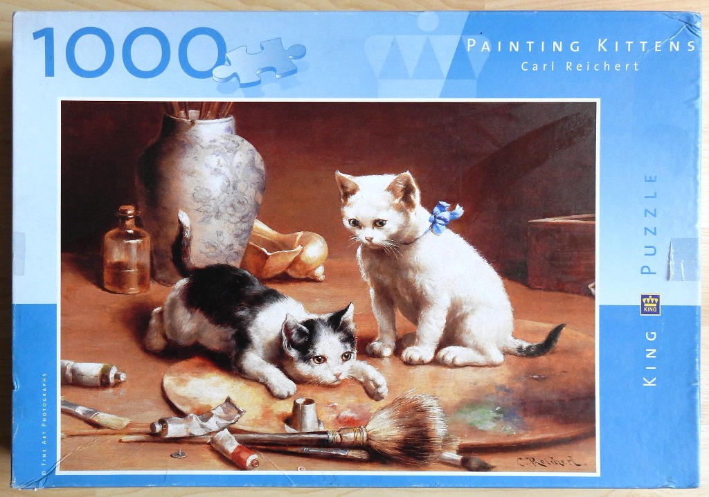 An oil painting of two kittens playing among artist supplies on a wooden surface.