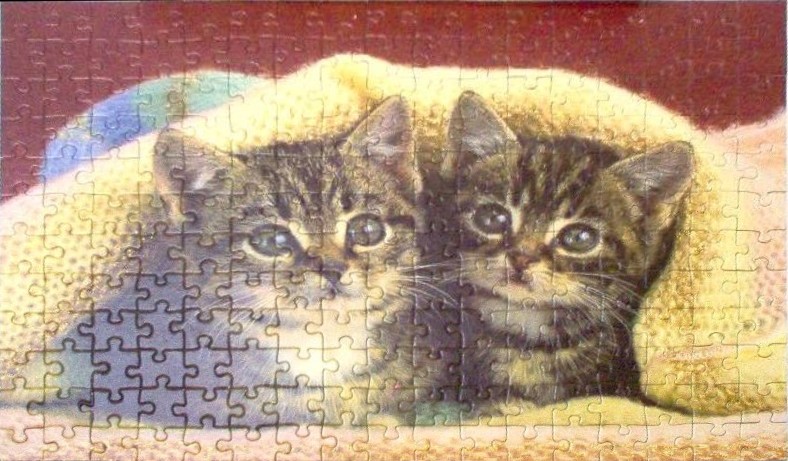 Two tabby kittens peeking out from under a soft yellow blanket against a deep red background.