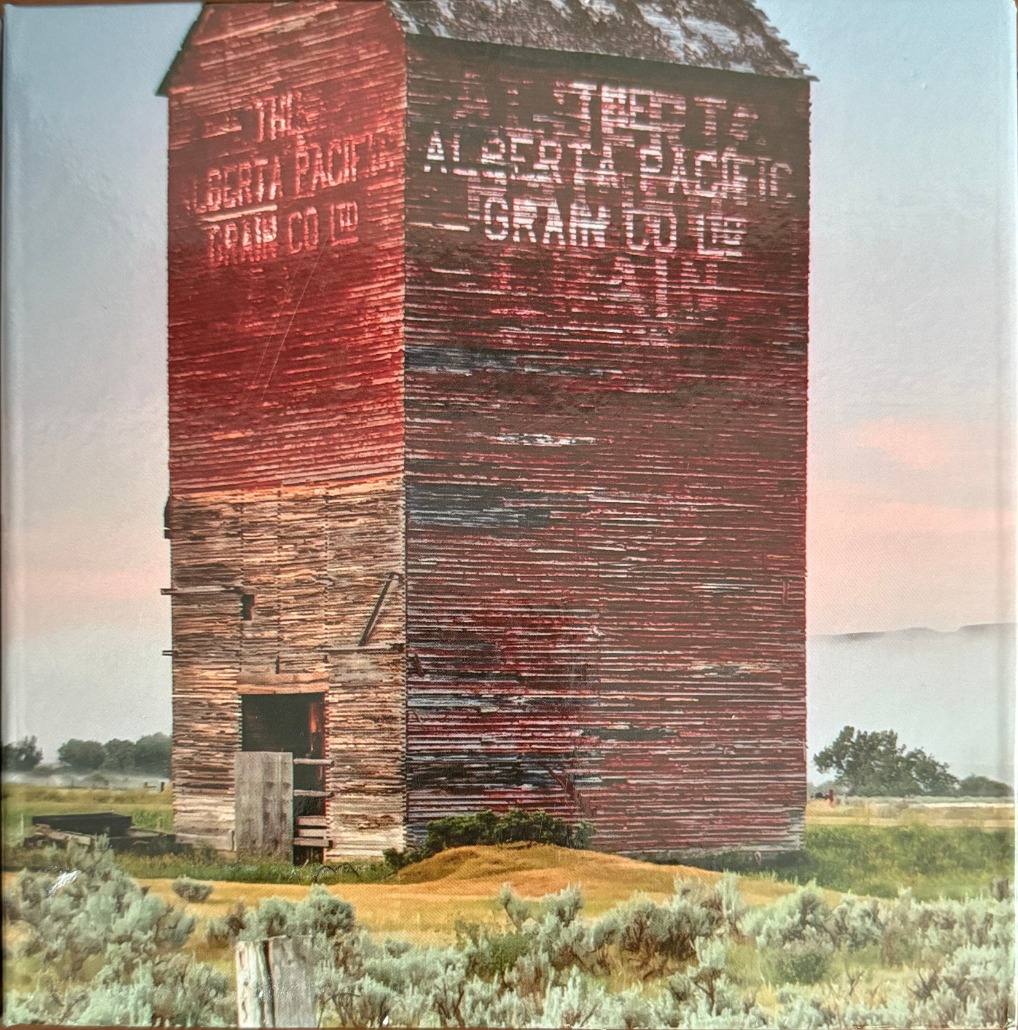 An old weathered red grain elevator stands in a rural landscape at dawn.