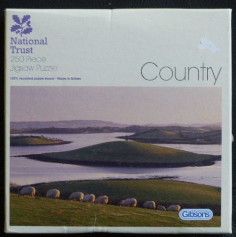 A scenic photograph of a line of sheep grazing on a green hillside overlooking calm coastal waters and small islands.