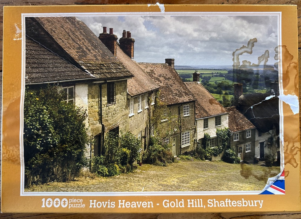 A view of the iconic cobblestone Gold Hill in Shaftesbury, lined with historic stone cottages overlooking the countryside.
