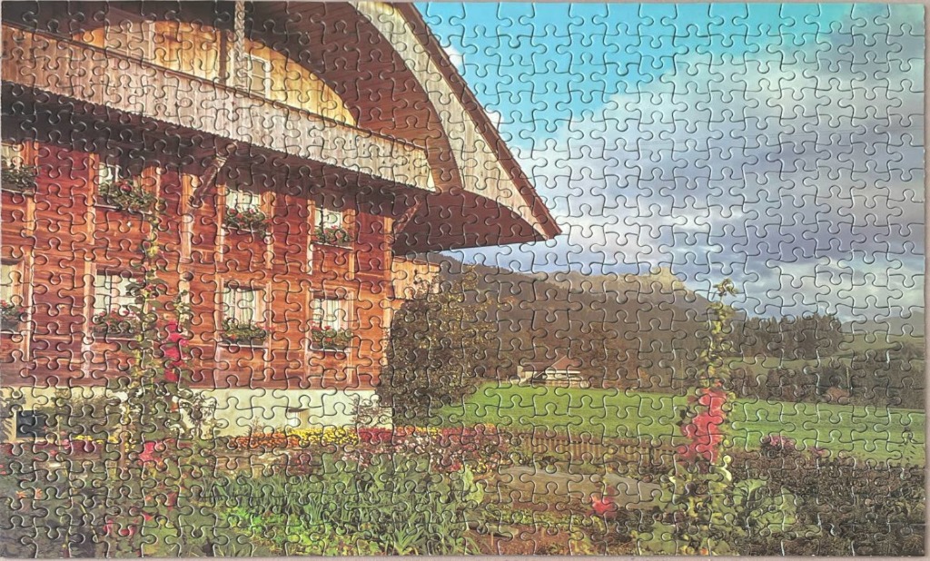 A traditional wooden Alpine chalet house set in a lush garden with mountains in the background.