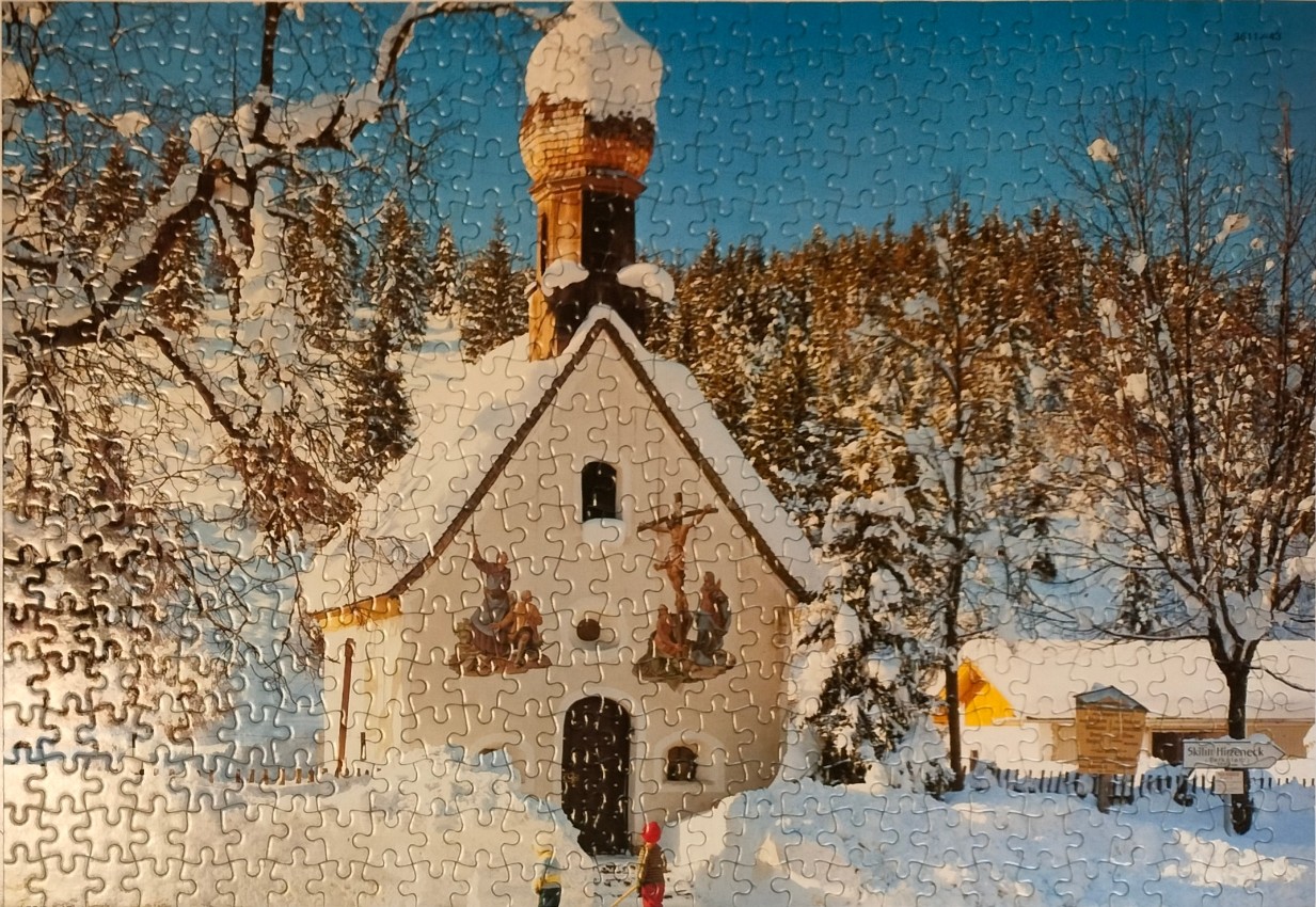 A small chapel in a snow-covered mountain landscape under a bright blue sky.