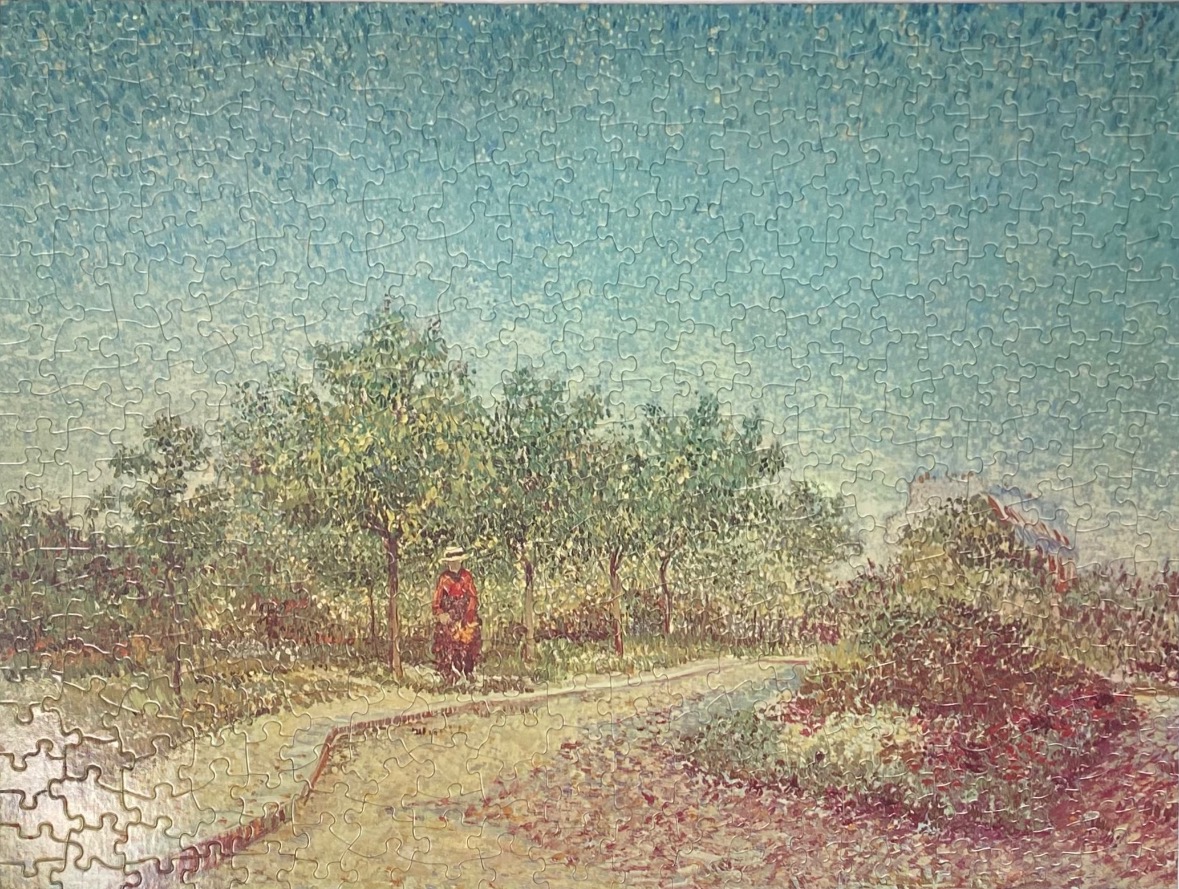 A woman in a red dress walks along a path in a park with light green trees under a pale blue sky.