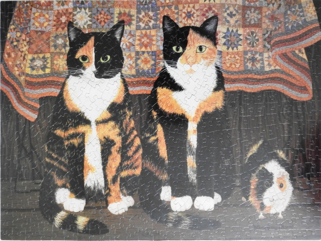 Two calico cats and a guinea pig sitting in front of a colorful patchwork quilt