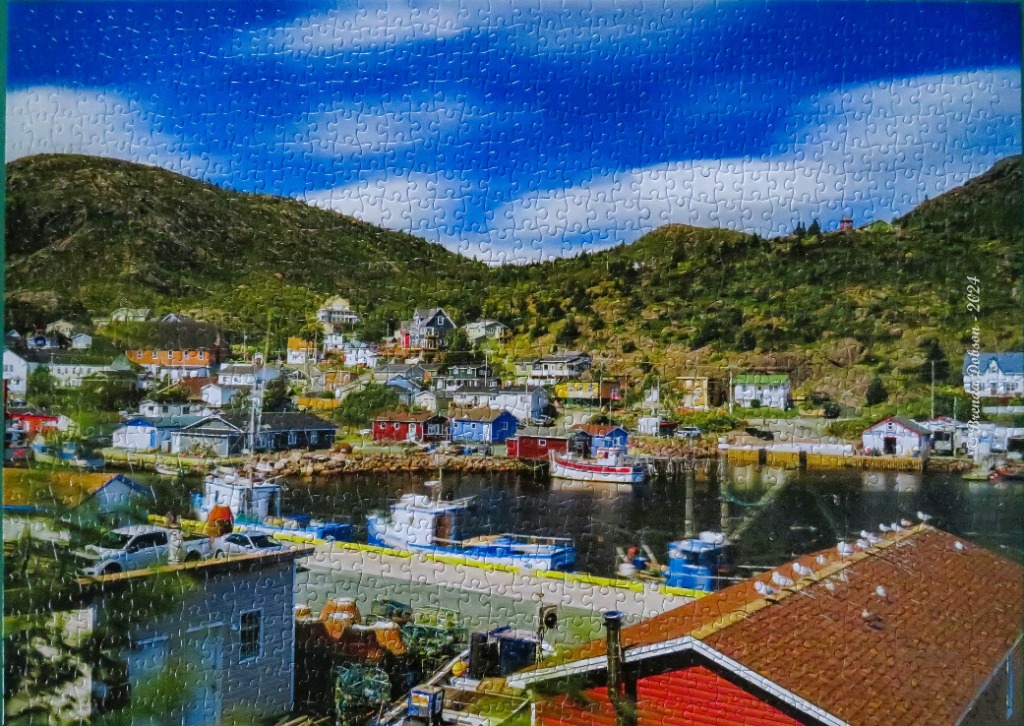A coastal village nestled in a green valley beside a harbor with small boats, under a bright blue sky.