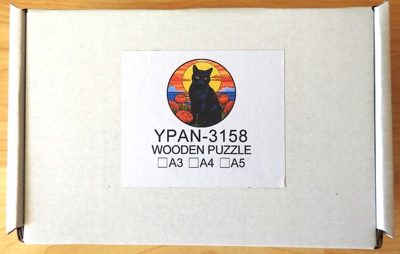 A digital illustration of a black cat sitting in front of a setting sun and orange flowers inside a circular frame.