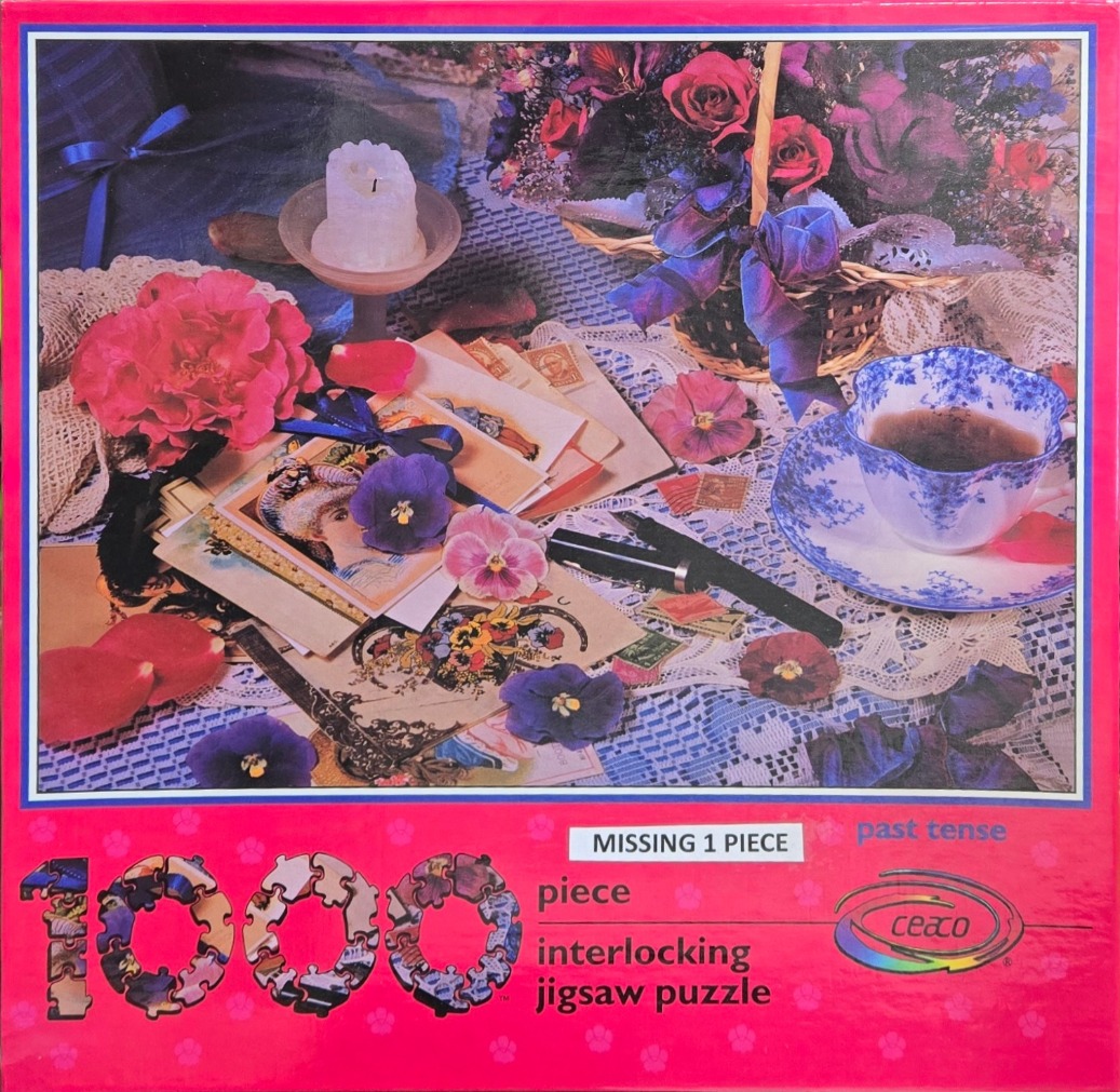 A still life featuring vintage postcards, a floral teacup, pansies, and a basket of roses on a lace tablecloth.