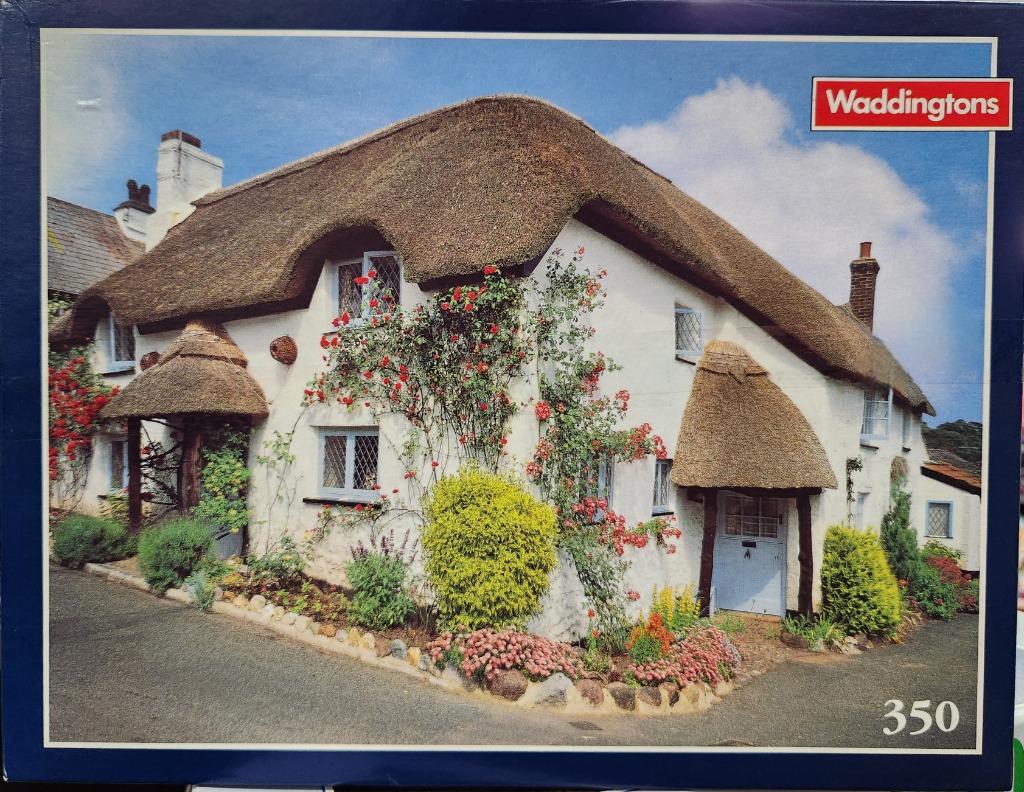 A charming white English cottage with a thatched roof and climbing red roses.