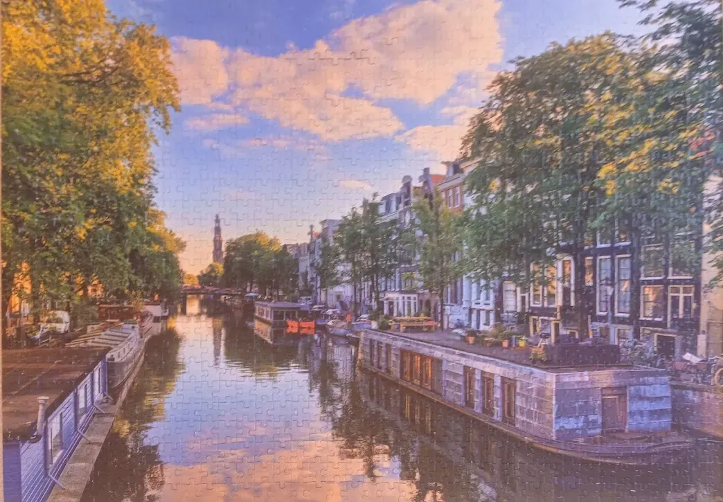 A peaceful Amsterdam canal scene at sunset with houseboats and historic buildings.