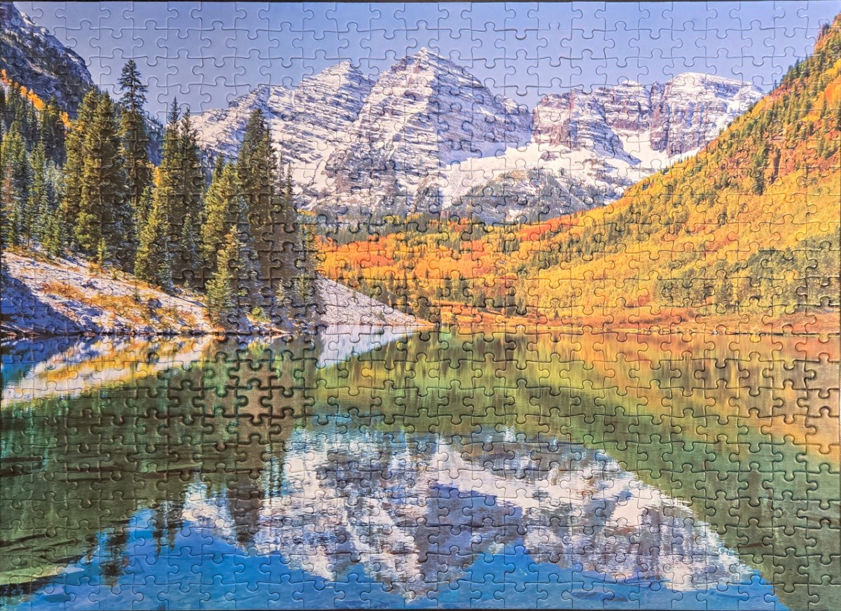 Snow-capped mountain peaks reflect in a serene lake surrounded by autumn foliage.