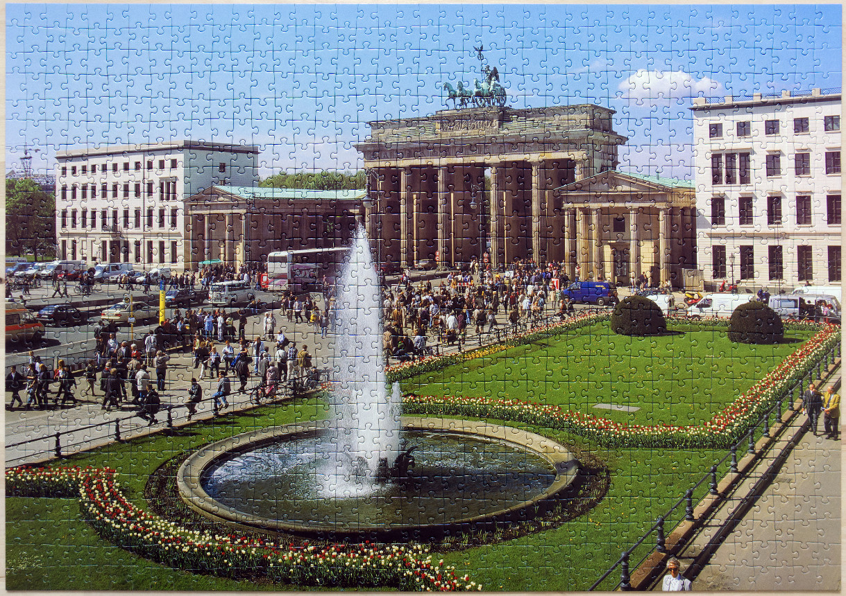 A sunny day at the Brandenburg Gate in Berlin with a central fountain and flower beds in the foreground.