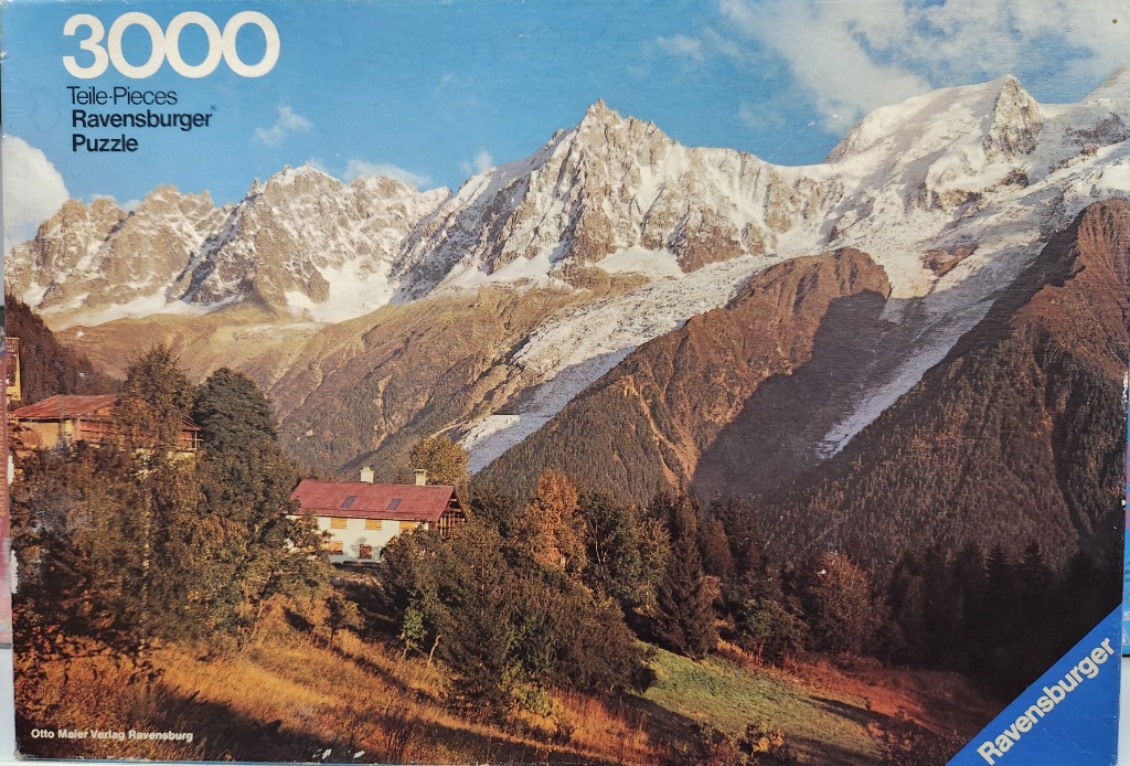 A photograph of a Swiss-style chalet nestled in a forested mountain valley with a large snow-capped peak behind it.