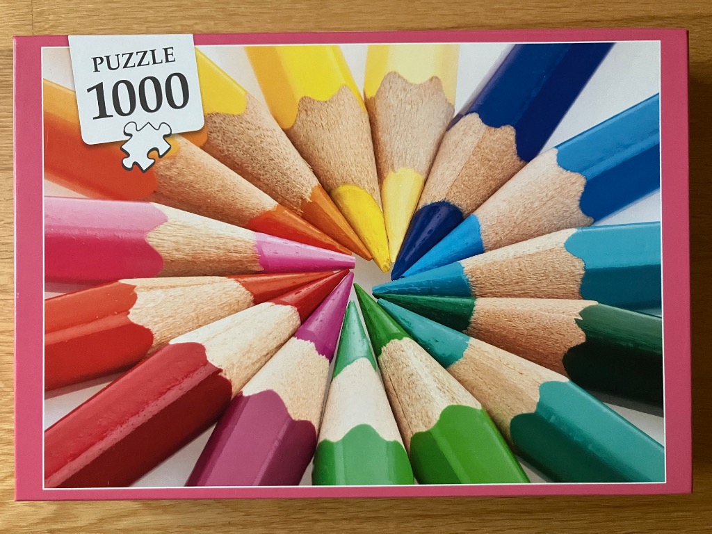 A top-down circular arrangement of sharpened colored pencils in a vibrant spectrum against a white background.