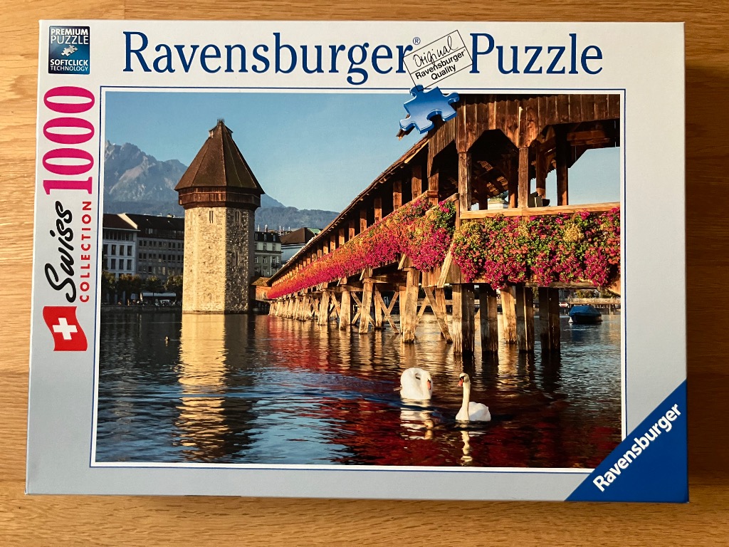 A photograph of the Chapel Bridge in Lucerne, Switzerland, featuring a stone tower, covered wooden bridge, and two swans.