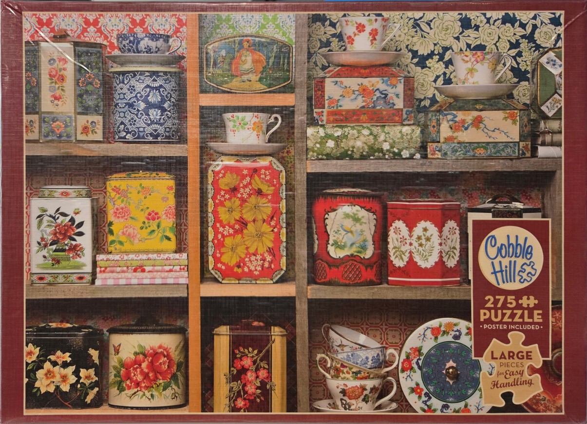 A collection of vintage floral tea tins and porcelain teacups arranged on wooden shelves with patterned wallpaper backgrounds