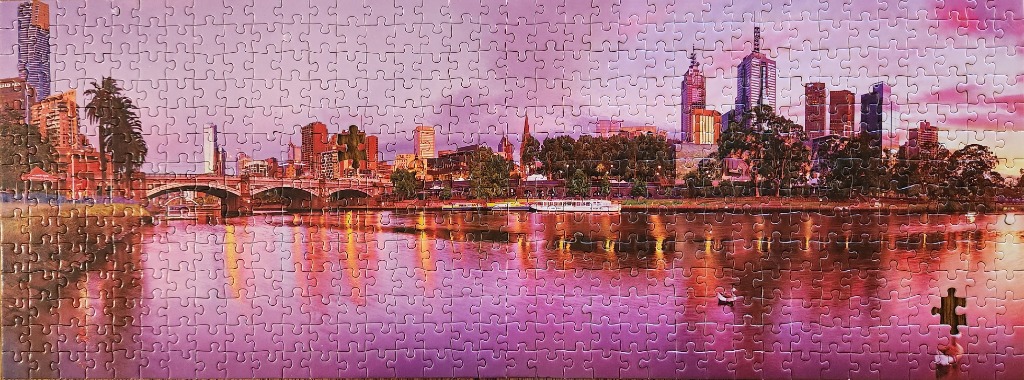 Panoramic view of a city skyline reflected in a river at twilight with pink and purple hues.