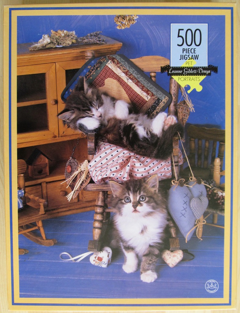 Two fluffy kittens with brown and white tabby markings in a rustic room with a miniature wooden rocking chair.