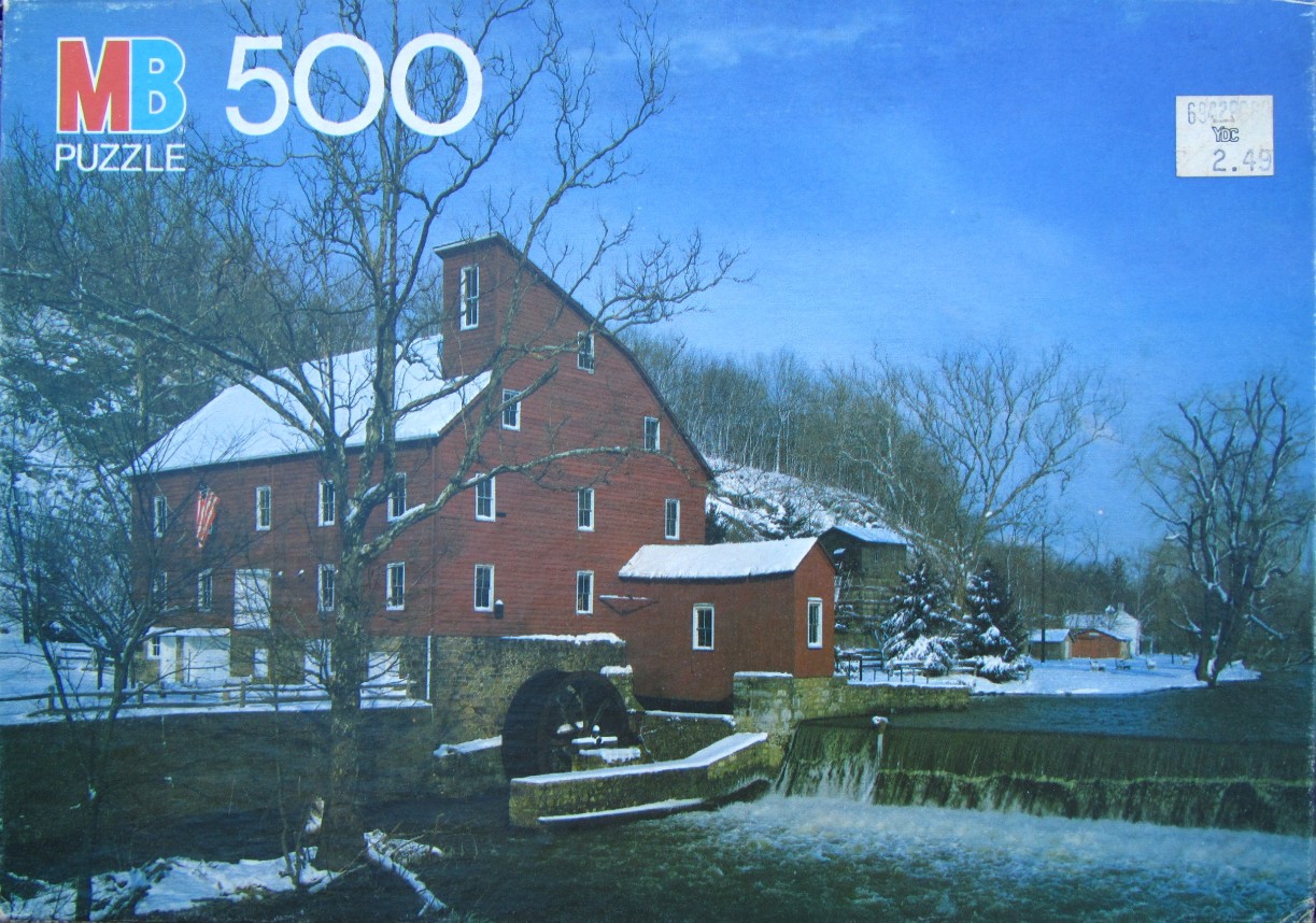 A rustic red grist mill covered in snow sits beside a waterfall and river in winter.