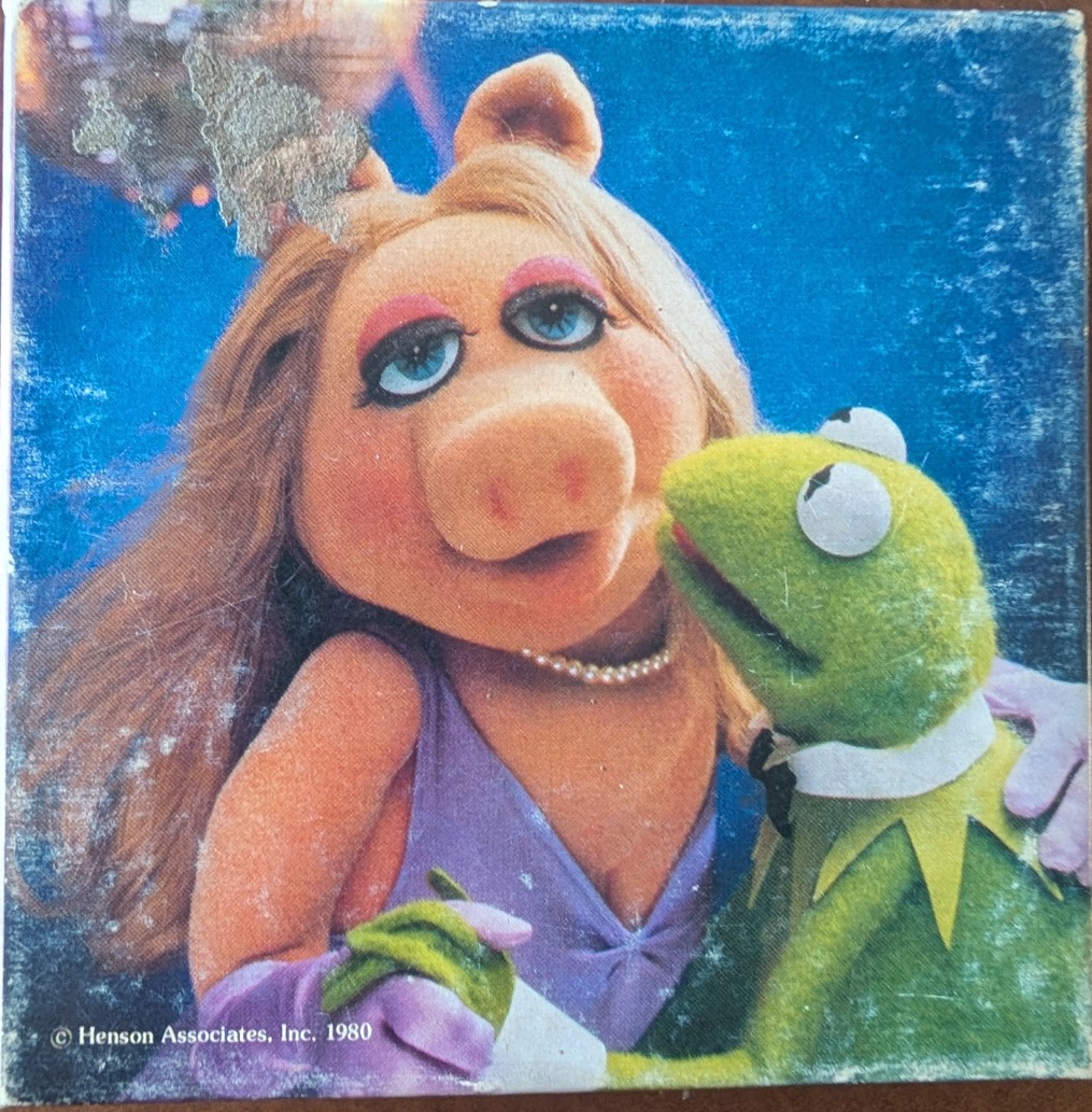 Miss Piggy and Kermit the Frog posing together in a studio setting against a blue background.