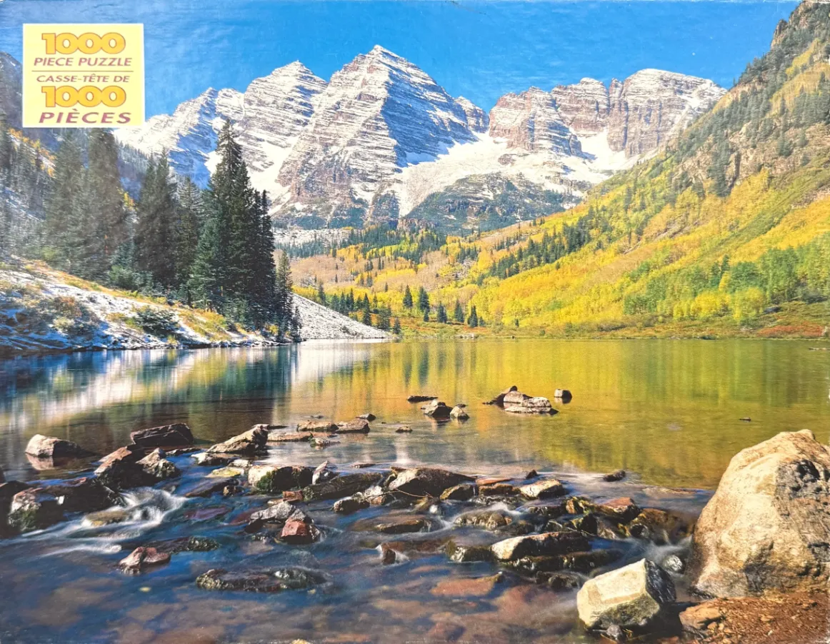 Scenic photograph of the Maroon Bells peaks reflecting in a lake surrounded by autumn foliage and snow.