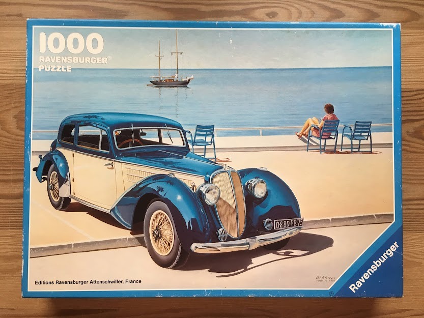 Vintage blue and cream luxury car parked on a seaside promenade with a woman sitting by the water.
