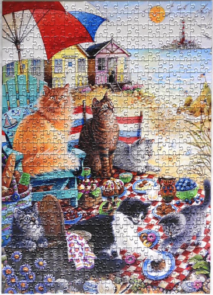 An illustration of several cats having a seaside picnic in front of colorful beach huts.