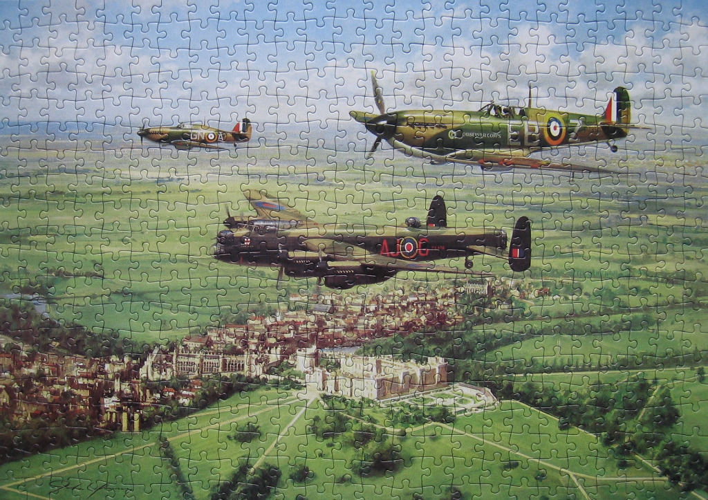 Painting of a Lancaster bomber flying over an English town with two Spitfires in the sky.