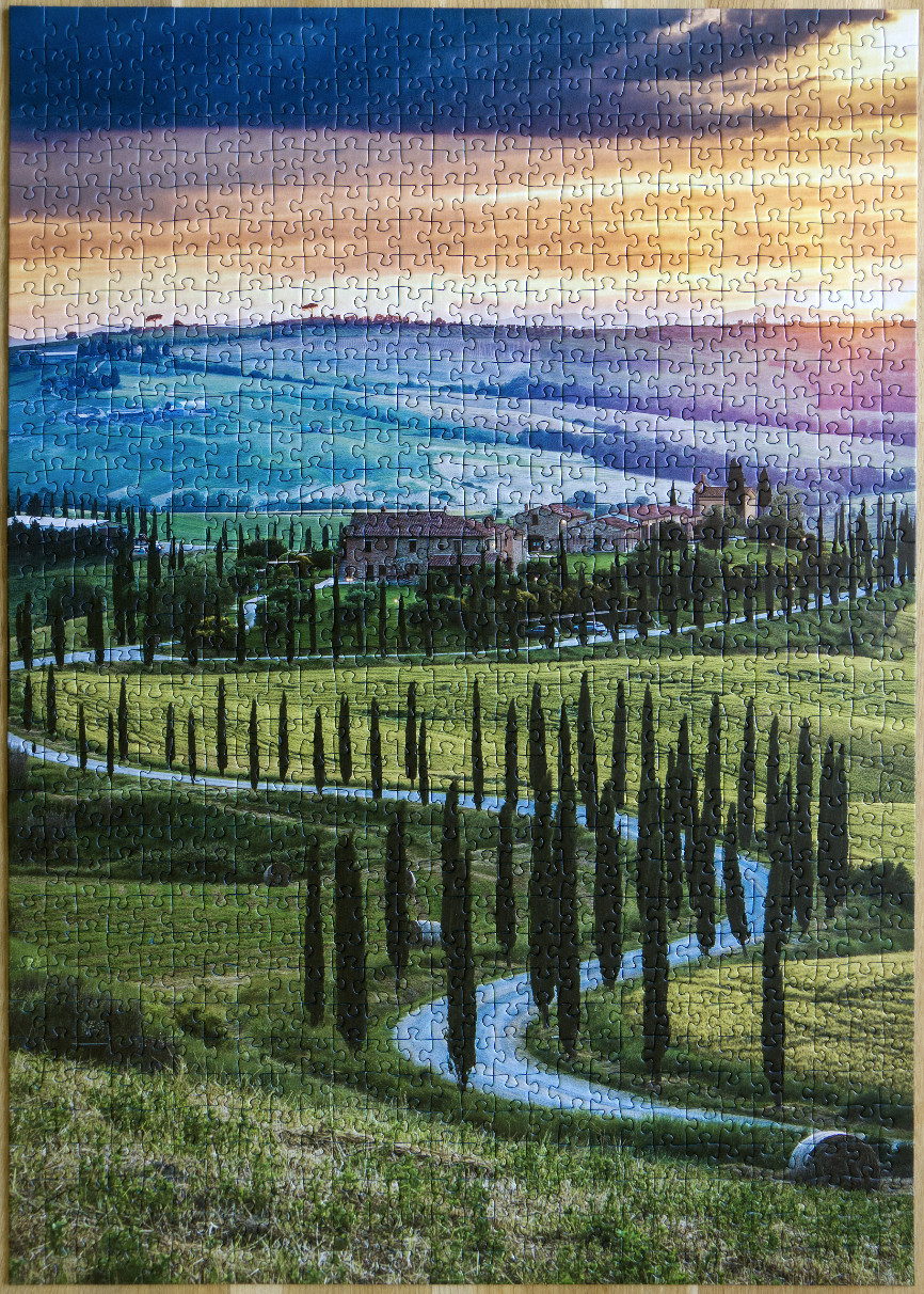 A photograph of a winding road lined with cypress trees leading to a stone villa in a rolling Tuscan landscape at sunset.