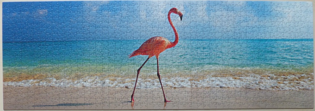A vibrant pink flamingo walks along a sandy tropical beach with a clear blue sea in the background.