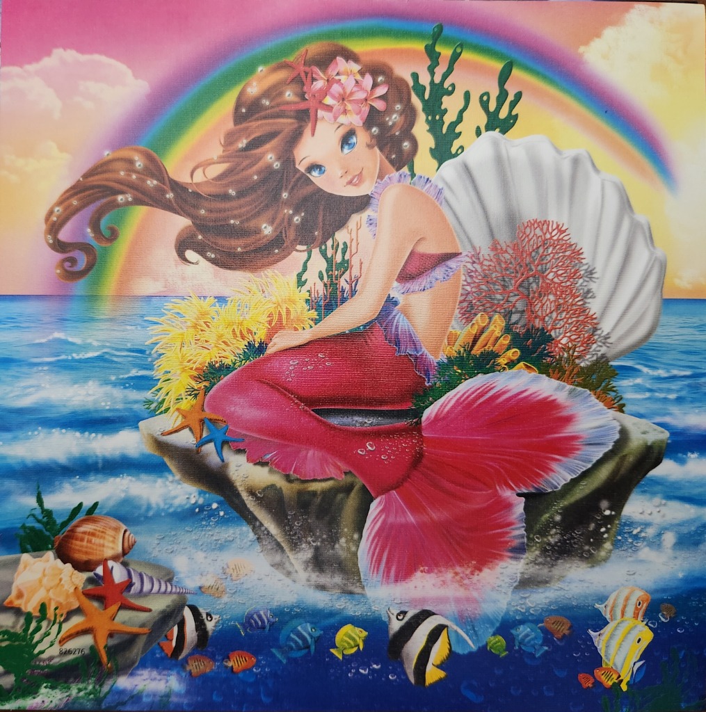A whimsical mermaid with brown hair and a pink tail sits on a rock in the ocean beneath a vibrant rainbow.
