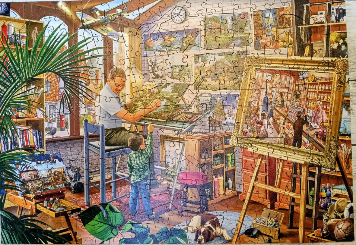 An elderly man painting at an easel while a young boy points at his work in a sunlit art studio.