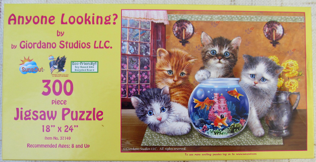 Three kittens sitting on a table in front of a fishbowl filled with goldfish and a decorative castle.