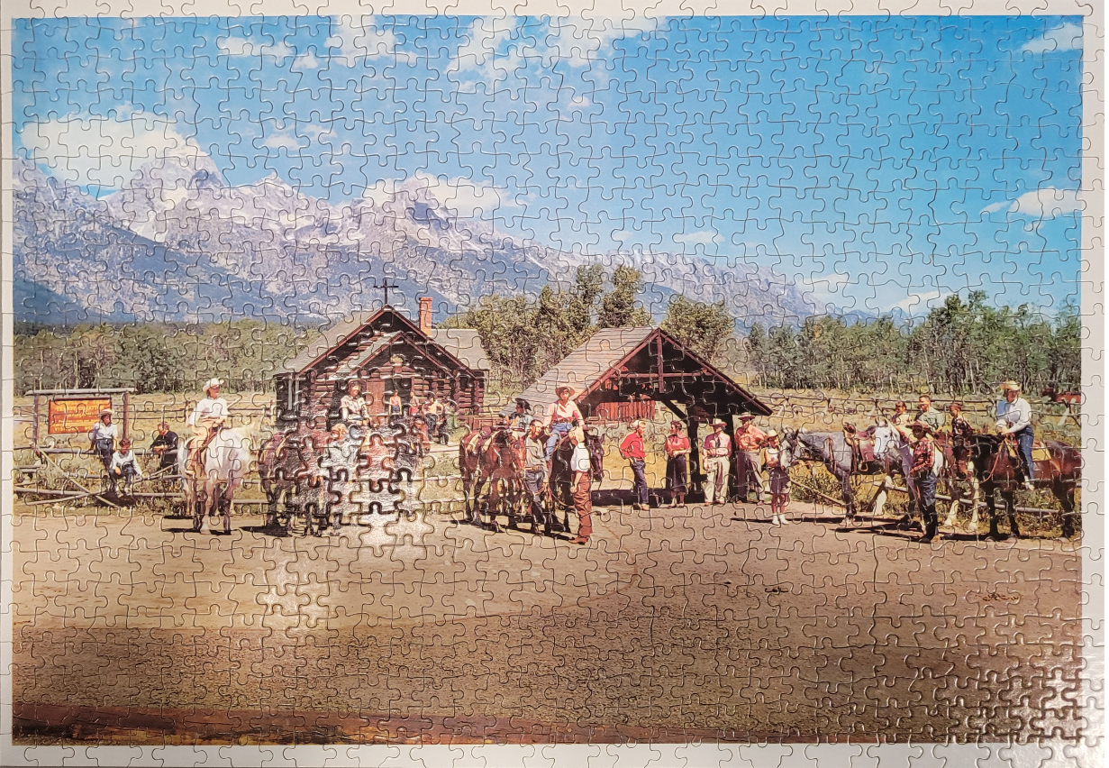 Western-themed landscape featuring a small log church, horses, and people in cowboy attire under a mountain range.
