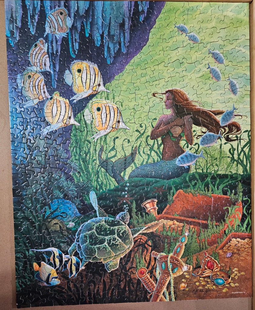 A mermaid swims near a sea turtle and treasure chest in an underwater scene with butterfly fish.