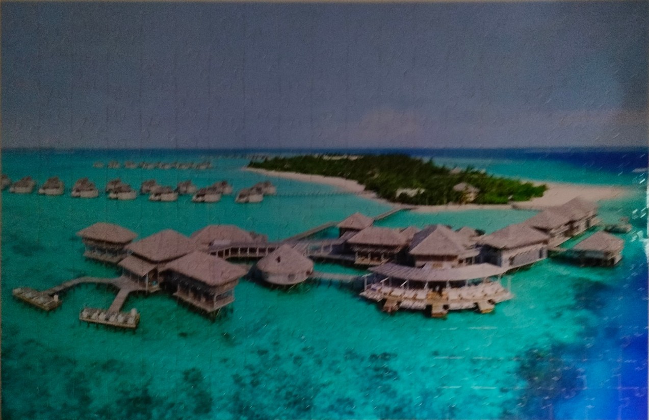 Aerial view of a tropical resort with overwater bungalows and a lush island in turquoise waters.
