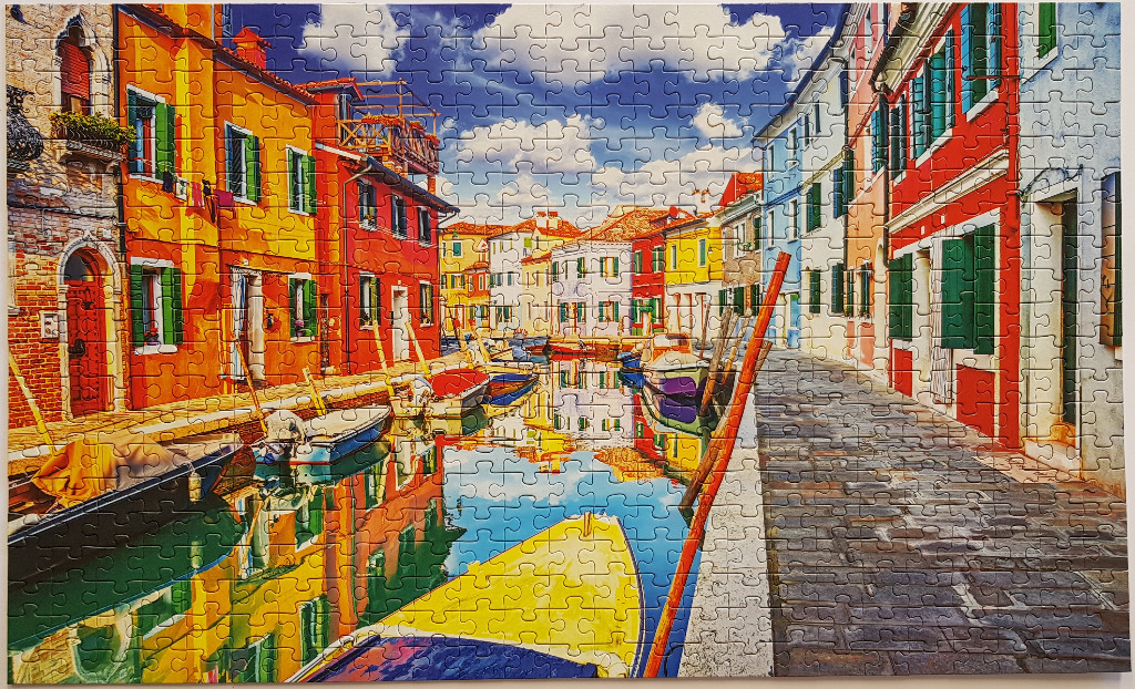 A vibrant canal scene in Burano, Italy, with colourful houses and small boats reflecting in the water.