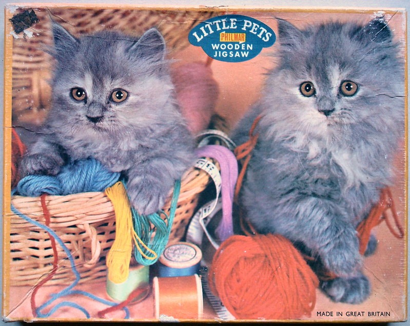 Two fluffy grey kittens sitting with wicker baskets and colorful balls of yarn.