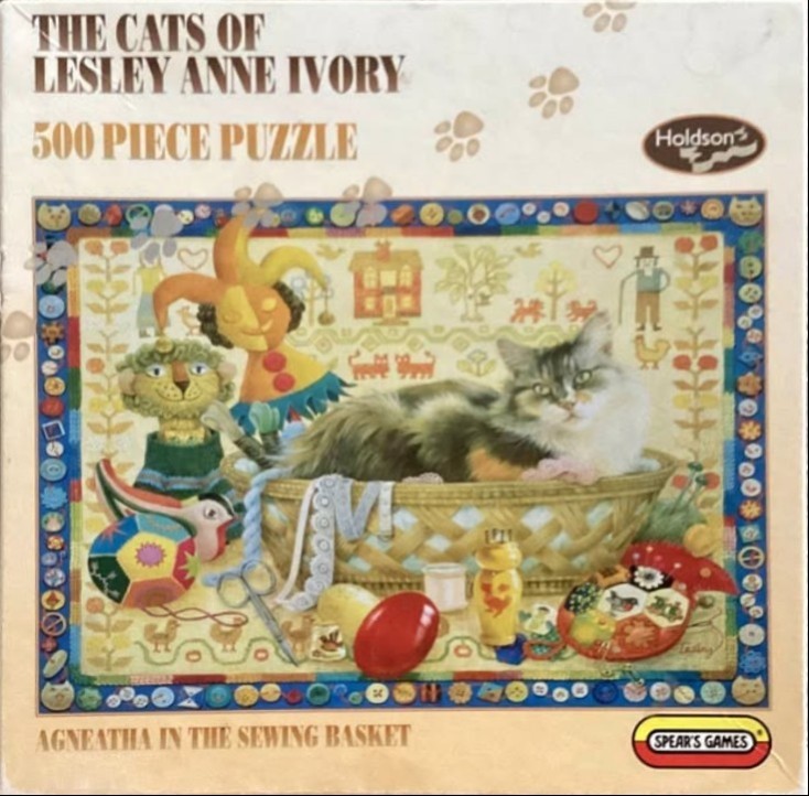 A long-haired cat resting inside a wicker sewing basket surrounded by craft supplies and a jester doll.