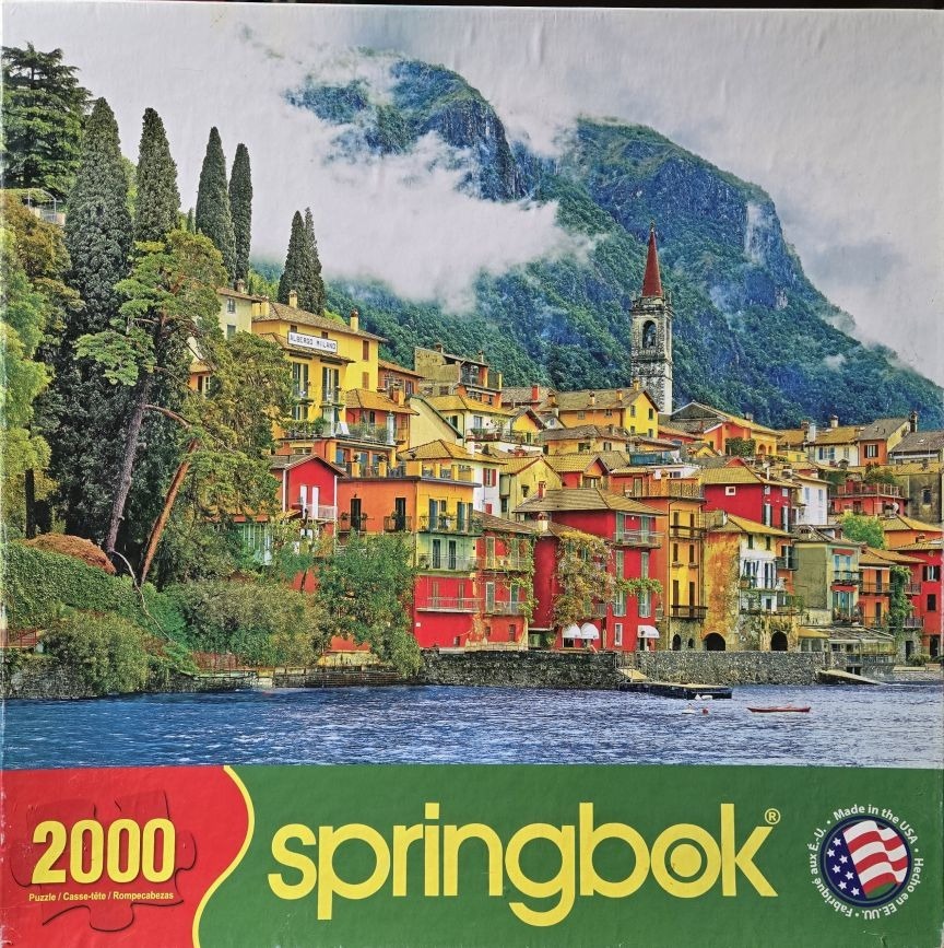 A picturesque Italian village nestled on a lake shore beneath towering, misty mountains.