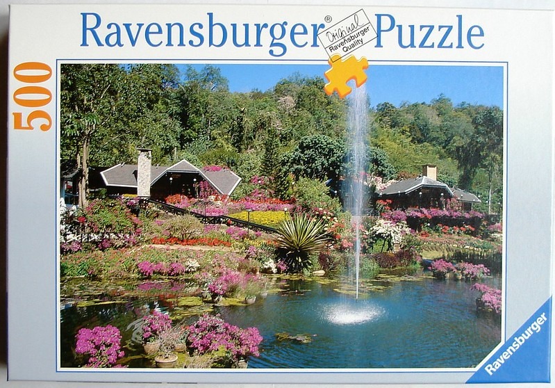 A lush garden scene with a central fountain, pond, flowering bushes, and wooden buildings in the background.