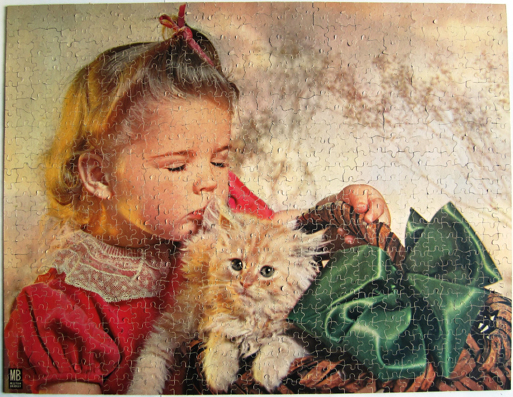 A young girl in a red dress kissing a fluffy orange kitten nestled in a basket with a large green bow.