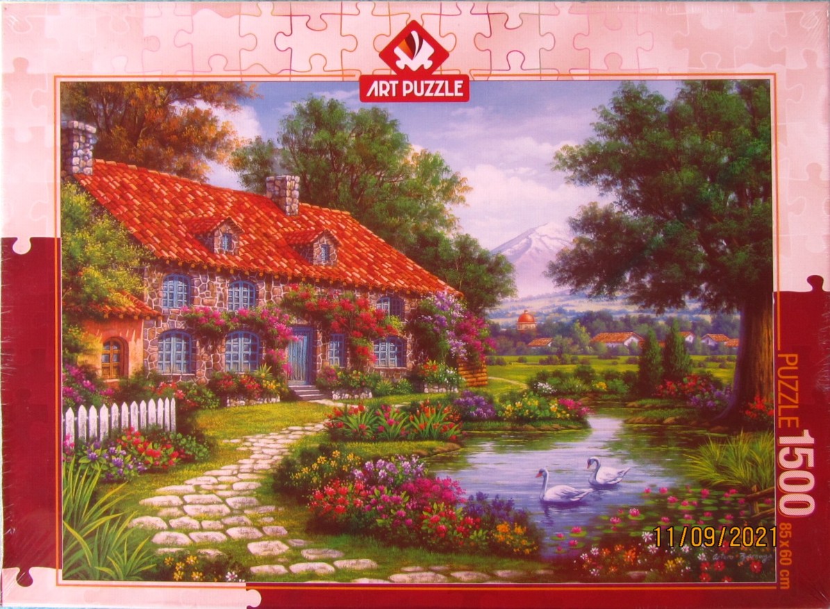An idyllic European-style stone cottage with a red tiled roof sits beside a pond with two swans in a lush garden.