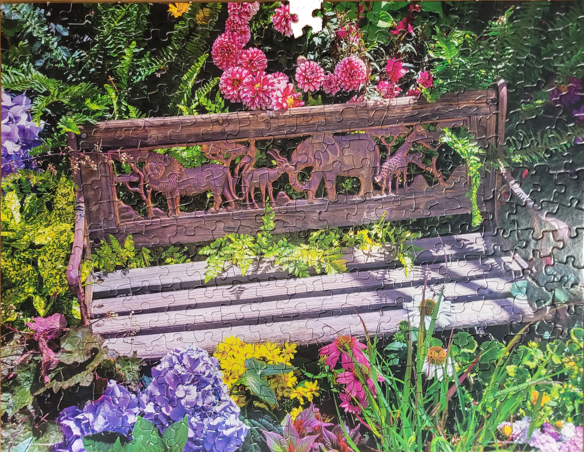A wooden garden bench decorated with safari animal carvings surrounded by lush, vibrant flowers.