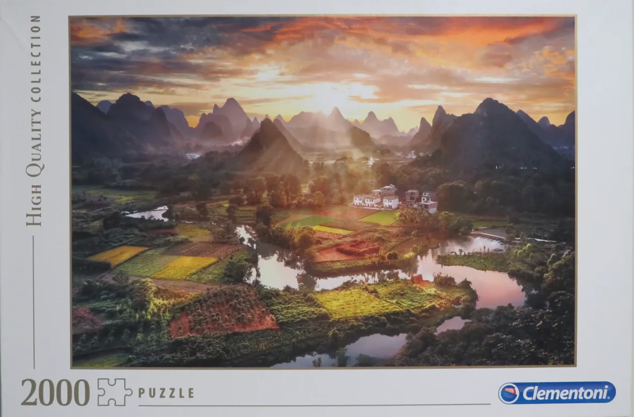 A scenic photograph of karst mountains, a winding river, and agricultural fields at sunset.